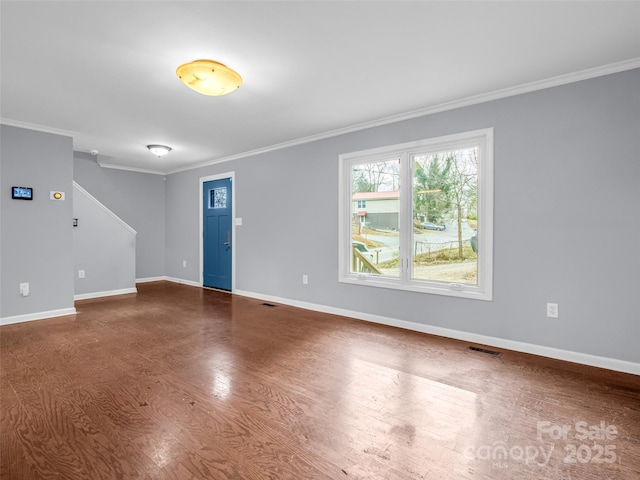 empty room with dark wood-style floors, baseboards, visible vents, and crown molding