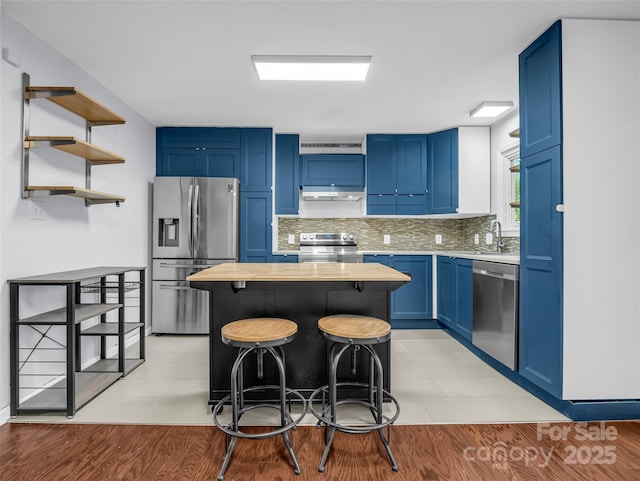 kitchen with a kitchen breakfast bar, under cabinet range hood, stainless steel appliances, blue cabinetry, and backsplash