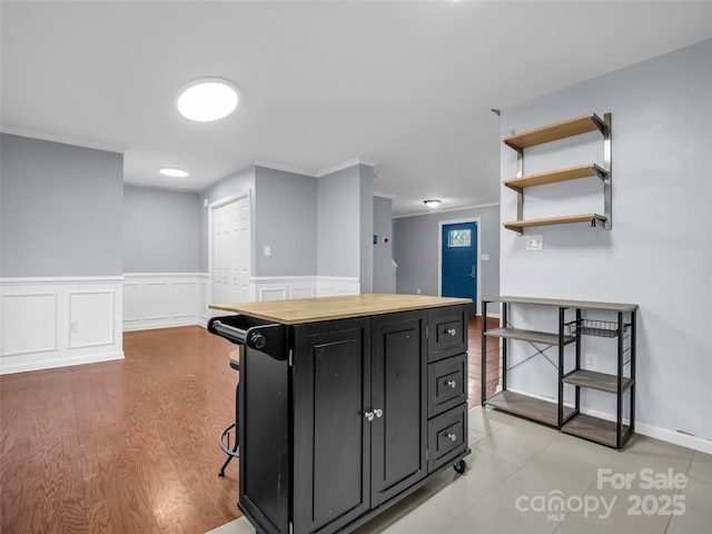 kitchen featuring crown molding, open shelves, butcher block countertops, light wood-type flooring, and dark cabinetry