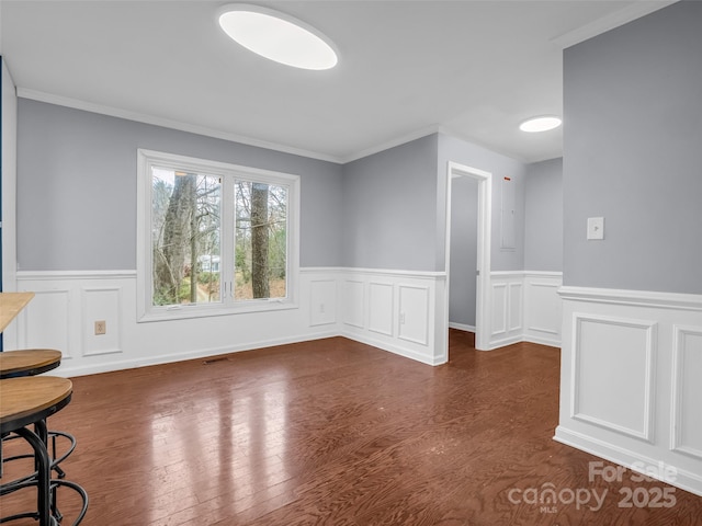 empty room with a wainscoted wall, wood finished floors, and crown molding