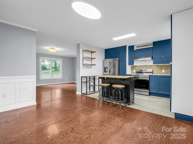 kitchen with a kitchen breakfast bar, blue cabinets, stainless steel appliances, light countertops, and under cabinet range hood