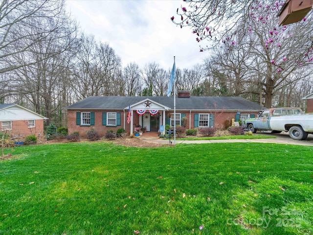 single story home featuring brick siding, a chimney, and a front yard