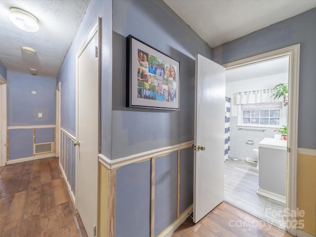 corridor featuring visible vents, a textured ceiling, and wood finished floors