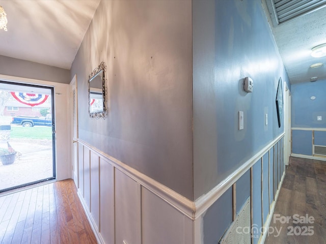 hallway with wainscoting, a decorative wall, and wood finished floors