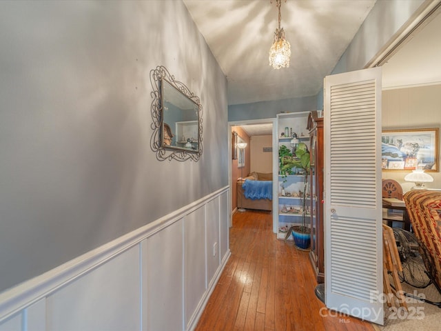 hall with a wainscoted wall, wood-type flooring, and a decorative wall