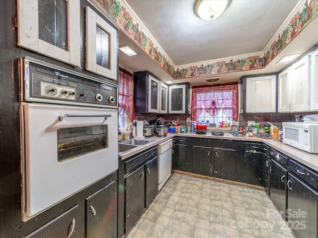 kitchen featuring dark cabinets, white appliances, a sink, light countertops, and tasteful backsplash