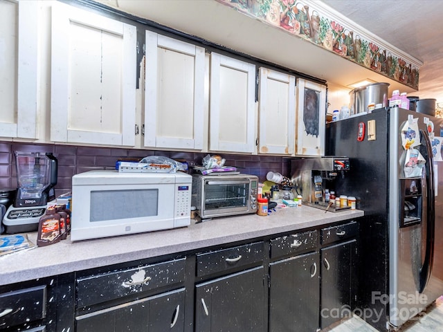 kitchen with white microwave, stainless steel refrigerator with ice dispenser, decorative backsplash, and light countertops