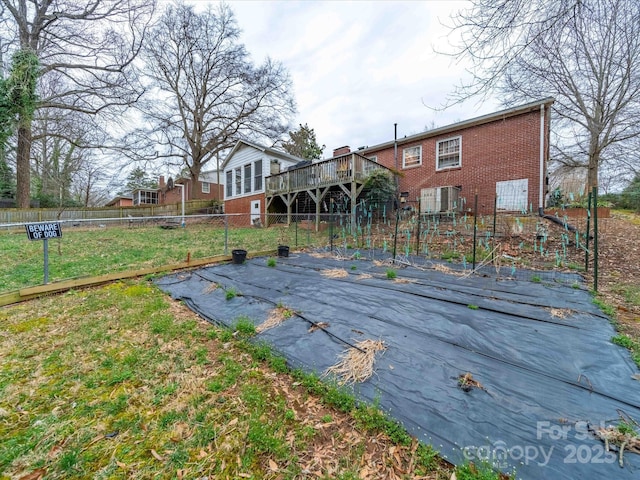 rear view of house with a deck, a yard, brick siding, and fence