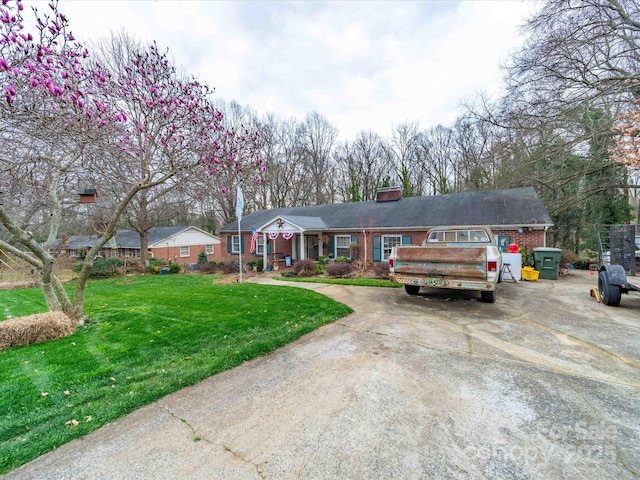 ranch-style house with concrete driveway, a front lawn, a chimney, and brick siding