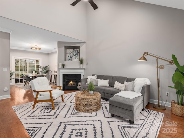 living area featuring a fireplace with flush hearth, ornamental molding, wood finished floors, and baseboards