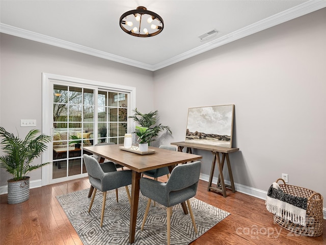 dining area with crown molding, a notable chandelier, wood-type flooring, visible vents, and baseboards