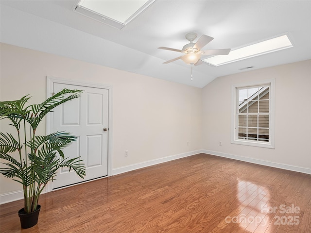 empty room with lofted ceiling with skylight, visible vents, baseboards, and wood finished floors