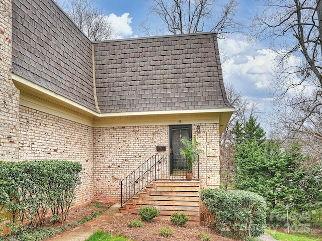 property entrance with brick siding, mansard roof, and roof with shingles