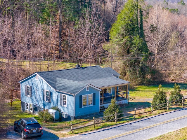 view of front of house featuring a forest view, a fenced front yard, covered porch, and a shingled roof