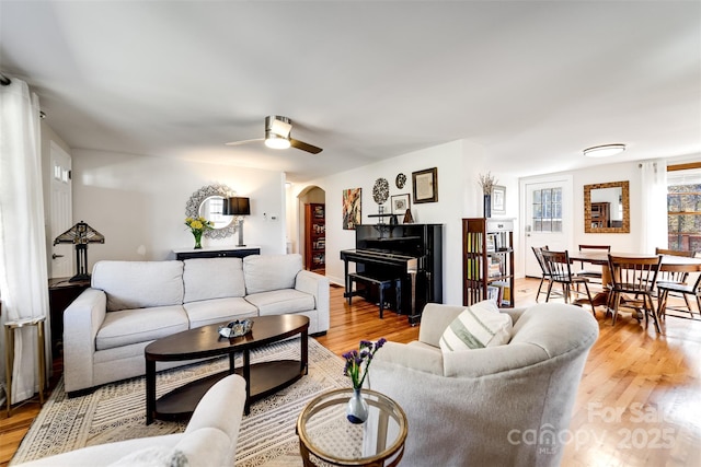 living area with arched walkways, ceiling fan, and light wood-style flooring