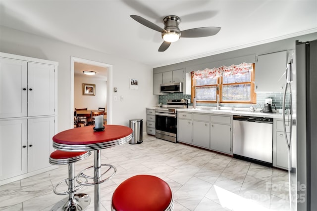 kitchen with tasteful backsplash, appliances with stainless steel finishes, marble finish floor, light countertops, and a sink