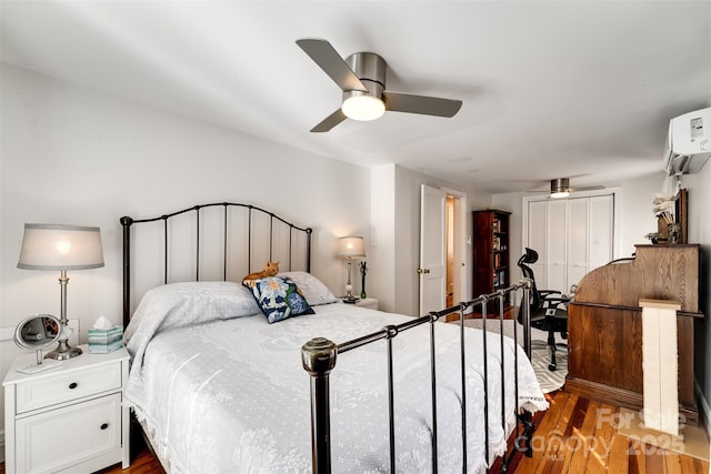 bedroom with ceiling fan, an AC wall unit, a closet, and wood finished floors