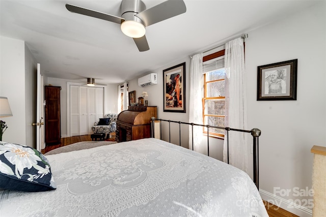 bedroom featuring baseboards, a wall unit AC, ceiling fan, wood finished floors, and a closet