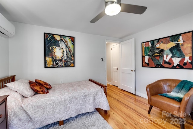 bedroom featuring a wall unit AC, ceiling fan, baseboards, and wood finished floors