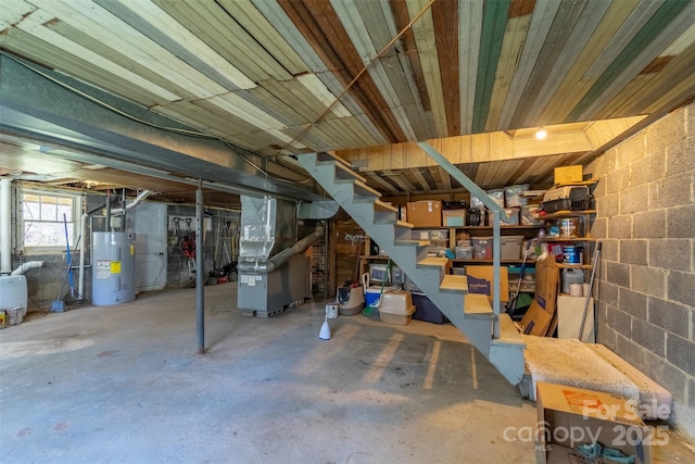 basement featuring heating unit, stairs, water heater, and concrete block wall