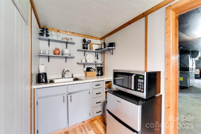 kitchen featuring open shelves, light countertops, stainless steel microwave, light wood-style floors, and a sink