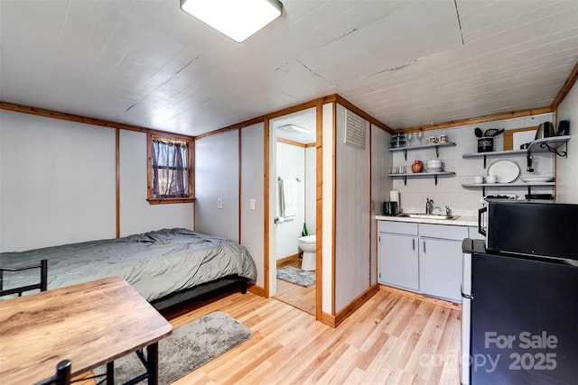 bedroom featuring light wood-type flooring, ensuite bath, a sink, and freestanding refrigerator