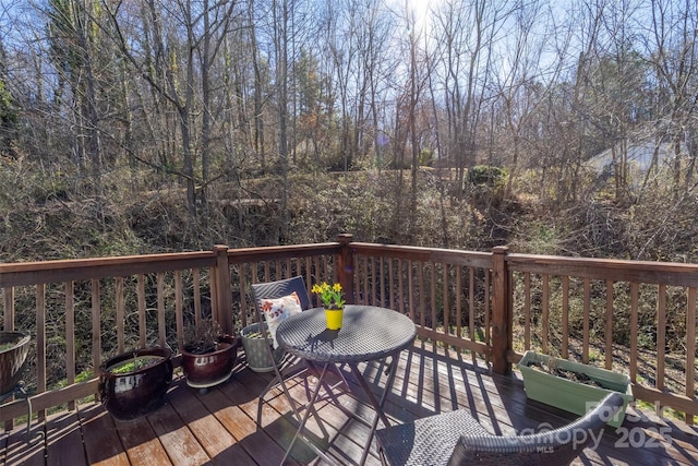 wooden terrace with a view of trees and outdoor dining space