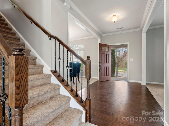 entryway with ornamental molding, visible vents, baseboards, and wood finished floors