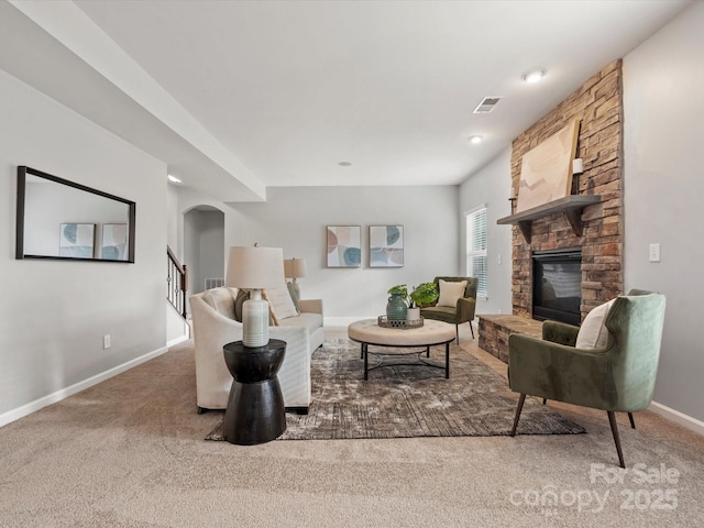 carpeted living room featuring baseboards, visible vents, arched walkways, stairway, and a stone fireplace