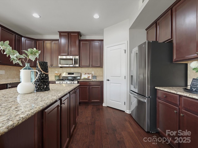 kitchen featuring tasteful backsplash, appliances with stainless steel finishes, dark wood finished floors, and light stone counters