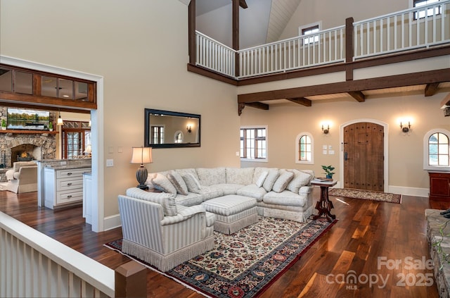 living area with dark wood-type flooring, a high ceiling, a fireplace, baseboards, and beam ceiling