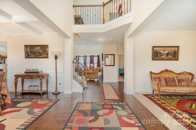 entrance foyer with beamed ceiling, wood finished floors, a towering ceiling, and stairway