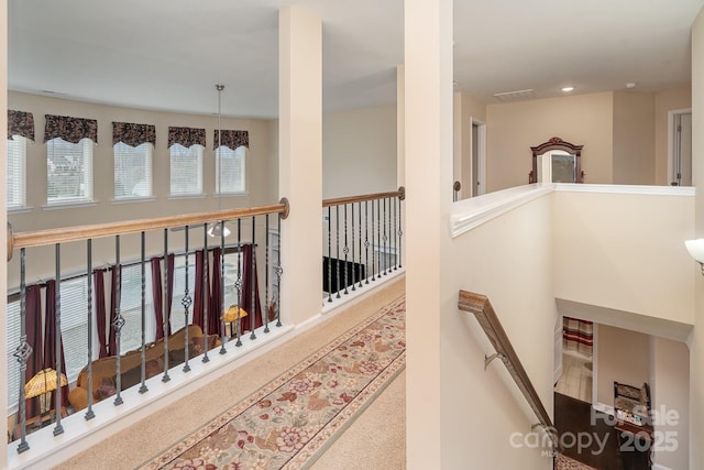 hallway with an upstairs landing, visible vents, and carpet floors