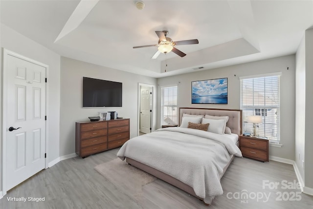 bedroom with light wood-type flooring, baseboards, visible vents, and a tray ceiling