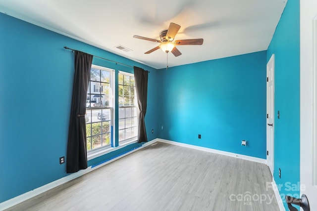 empty room with a ceiling fan, wood finished floors, visible vents, and baseboards