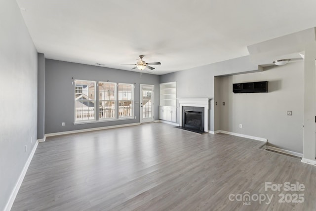 unfurnished living room with ceiling fan, wood finished floors, a high end fireplace, and baseboards