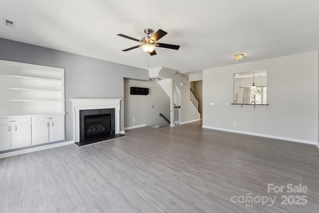 unfurnished living room featuring visible vents, stairway, a fireplace with flush hearth, wood finished floors, and baseboards