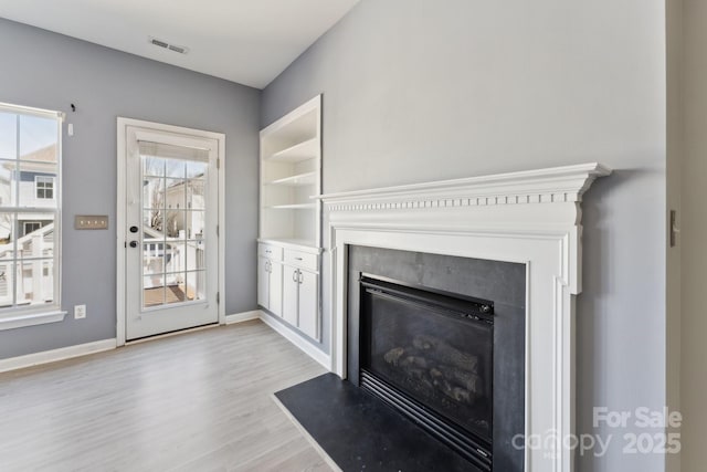 unfurnished living room with light wood-type flooring, a fireplace with flush hearth, visible vents, and baseboards