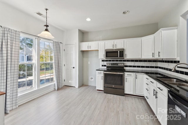 kitchen featuring stainless steel appliances, dark countertops, tasteful backsplash, visible vents, and a sink