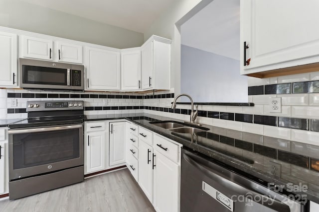 kitchen featuring appliances with stainless steel finishes, white cabinetry, a sink, and decorative backsplash