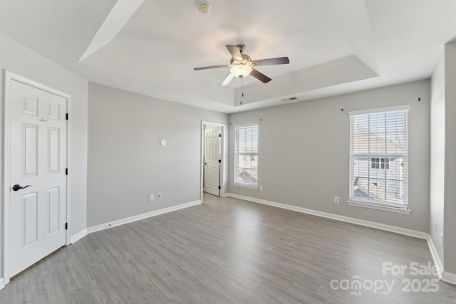 unfurnished bedroom featuring a tray ceiling, multiple windows, baseboards, and wood finished floors