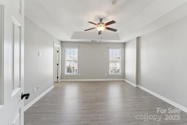 spare room with baseboards, a raised ceiling, a ceiling fan, and wood finished floors