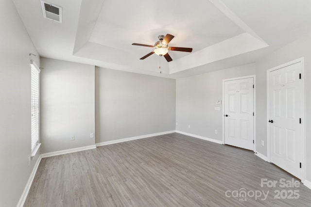 empty room with a tray ceiling, wood finished floors, visible vents, and baseboards