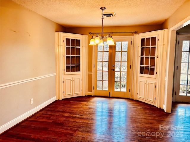 unfurnished dining area featuring a textured ceiling, dark wood-type flooring, baseboards, french doors, and an inviting chandelier