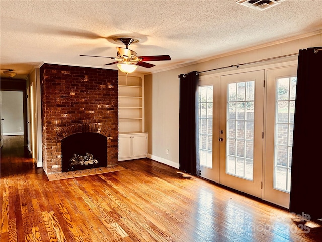 unfurnished living room with a brick fireplace, built in shelves, visible vents, and wood finished floors