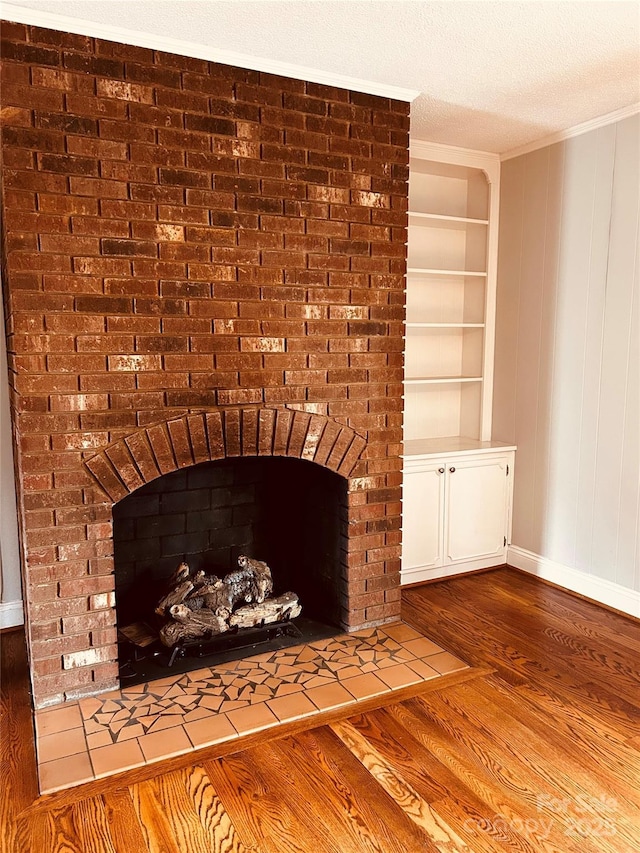 details featuring a textured ceiling, wood finished floors, built in features, ornamental molding, and a brick fireplace