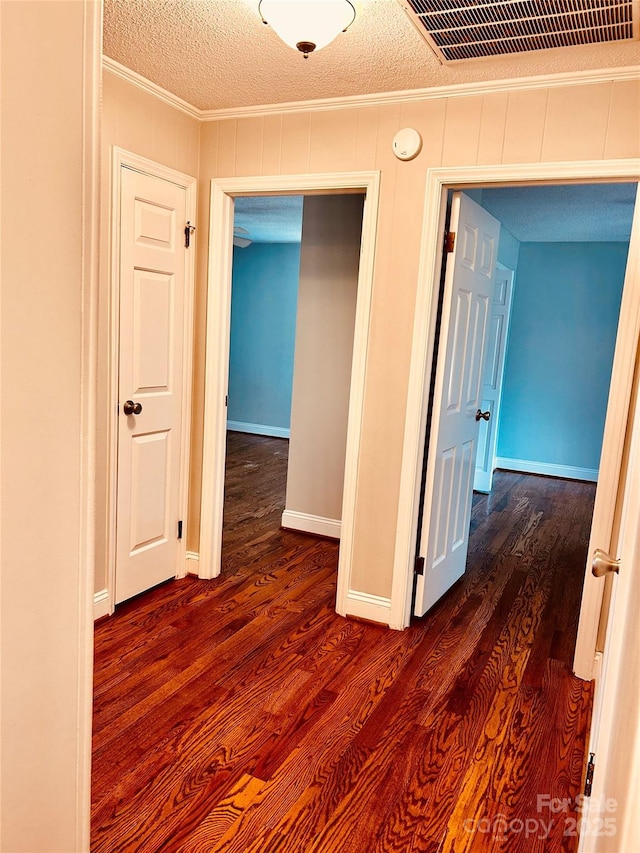 hallway with baseboards, visible vents, ornamental molding, dark wood-style flooring, and a textured ceiling