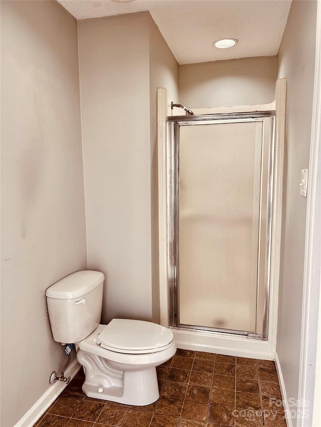 bathroom with a stall shower, baseboards, and toilet