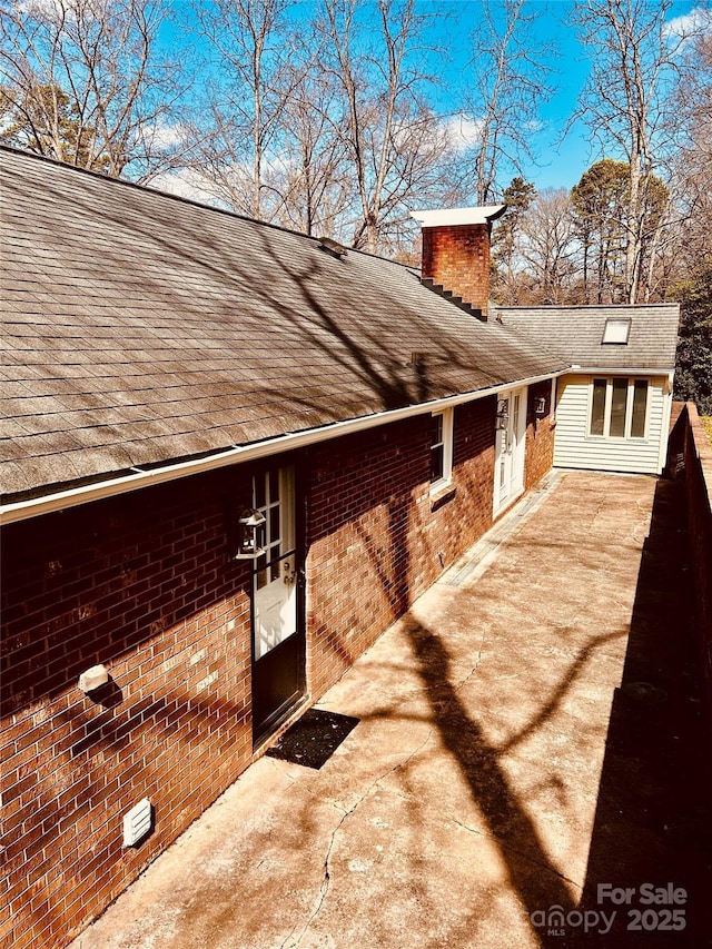 view of property exterior featuring brick siding, a chimney, and a shingled roof