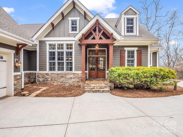 view of front of house featuring stone siding, french doors, board and batten siding, and roof with shingles